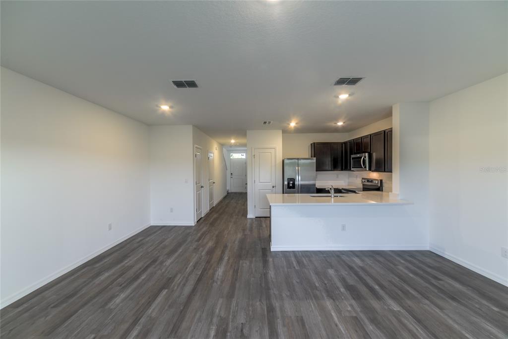 An open-concept kitchen with dark cabinets and a white island overlooks a living area — 17208 ENGLISH CHESTNUT WAY, LAND O LAKES, FL