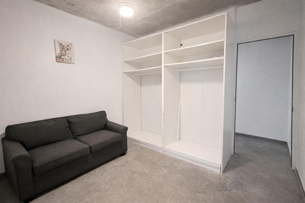 A room with a gray sofa, two white open closets, and unfinished concrete flooring — 45 BARCELONA, GUAYAMA, PR