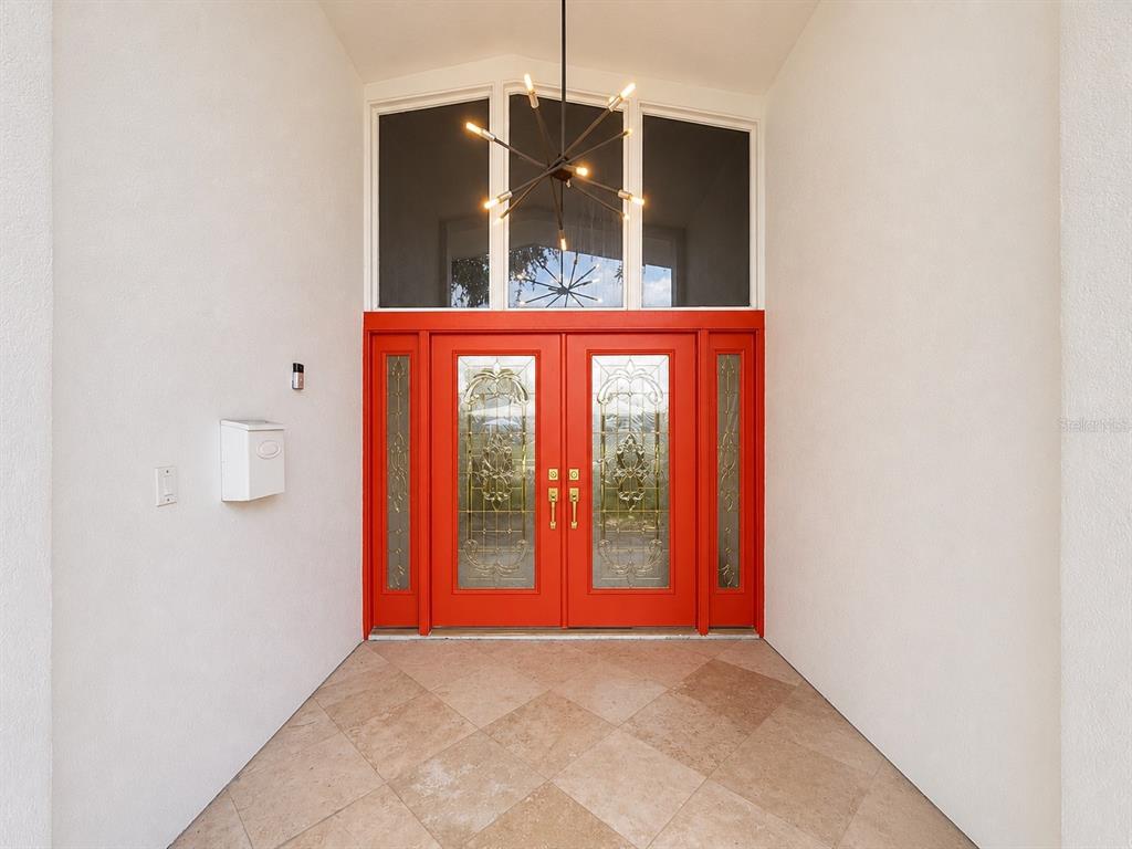 A bright red double front door with glass inserts sits under a modern chandelier — 217 YARMOUTH ROAD, CASSELBERRY, FL
