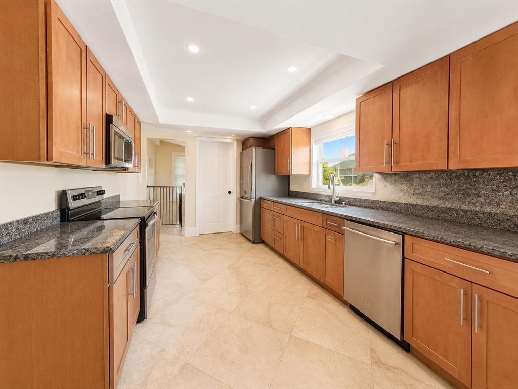A kitchen with wood cabinets, granite countertops, stainless steel appliances, and light-colored tile flooring — 217 YARMOUTH ROAD, CASSELBERRY, FL