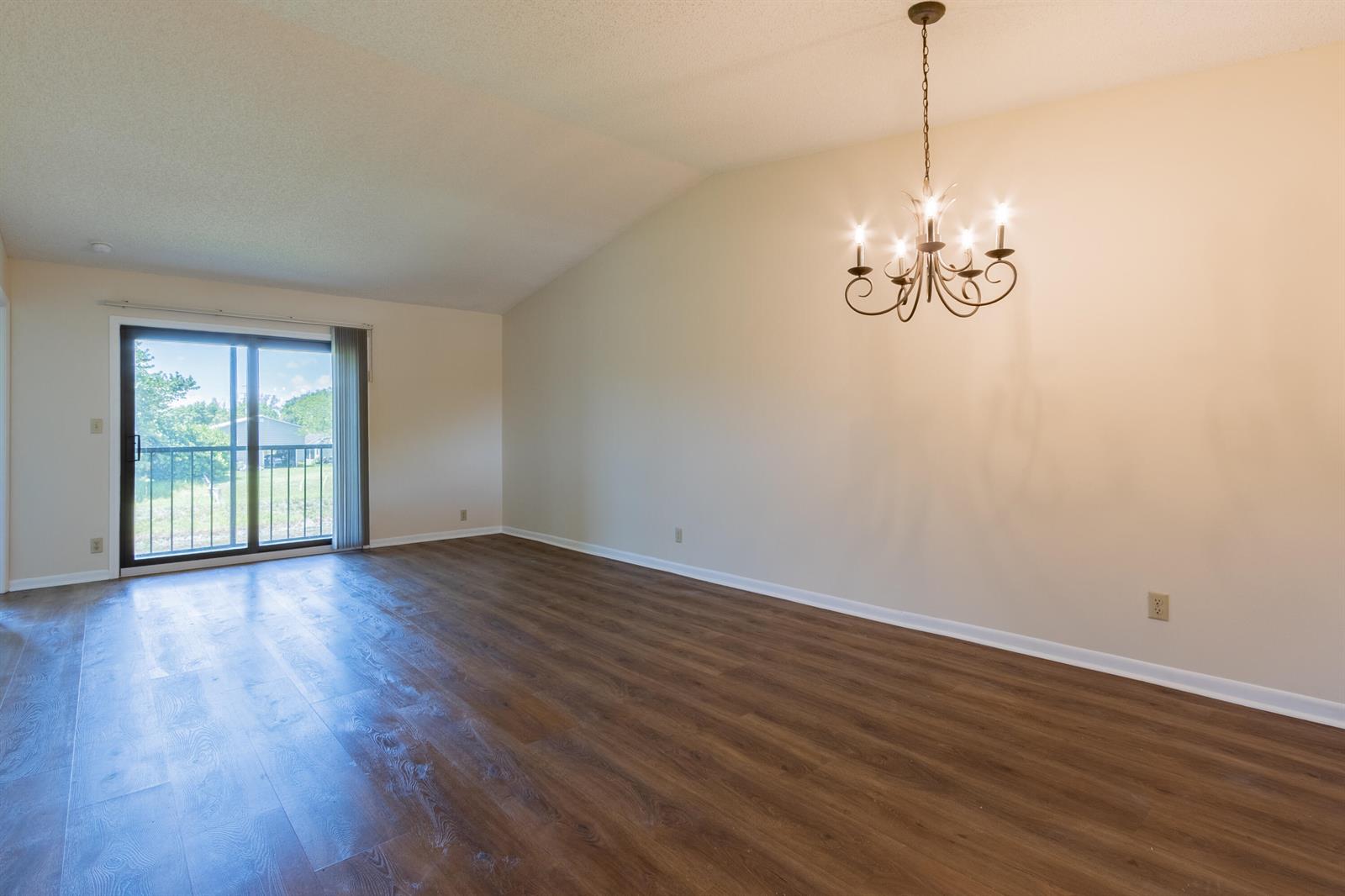 An empty room with wood-look flooring, a vaulted ceiling, a chandelier, and a sliding glass door — 9449 Boca Cove Circle # 911, Boca Raton FL 33428, BOCA RATON, FL