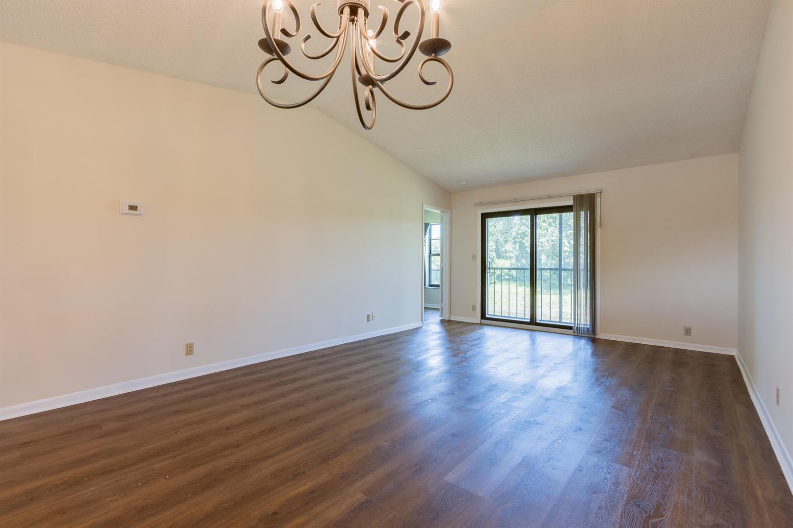 An empty living room features wood-look flooring, a vaulted ceiling, a chandelier, and sliding doors — 9449 Boca Cove Circle # 911, Boca Raton FL 33428, BOCA RATON, FL