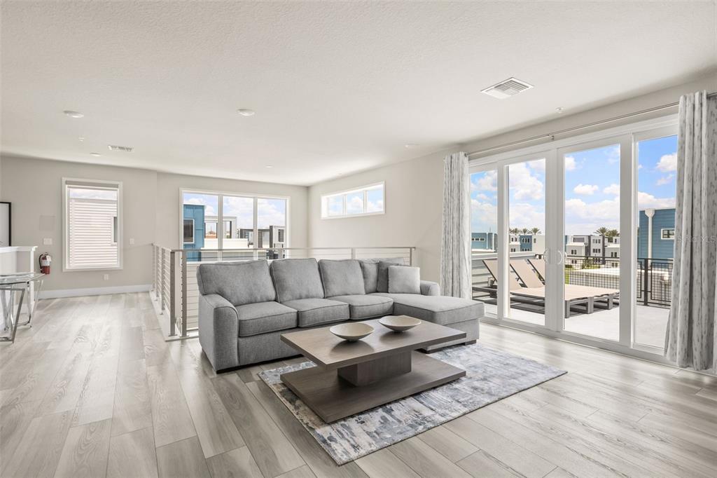 A modern living room features light wood floors, a gray sectional sofa, and a balcony — 7770 SANDY RIDGE DRIVE UNIT 227, REUNION, FL