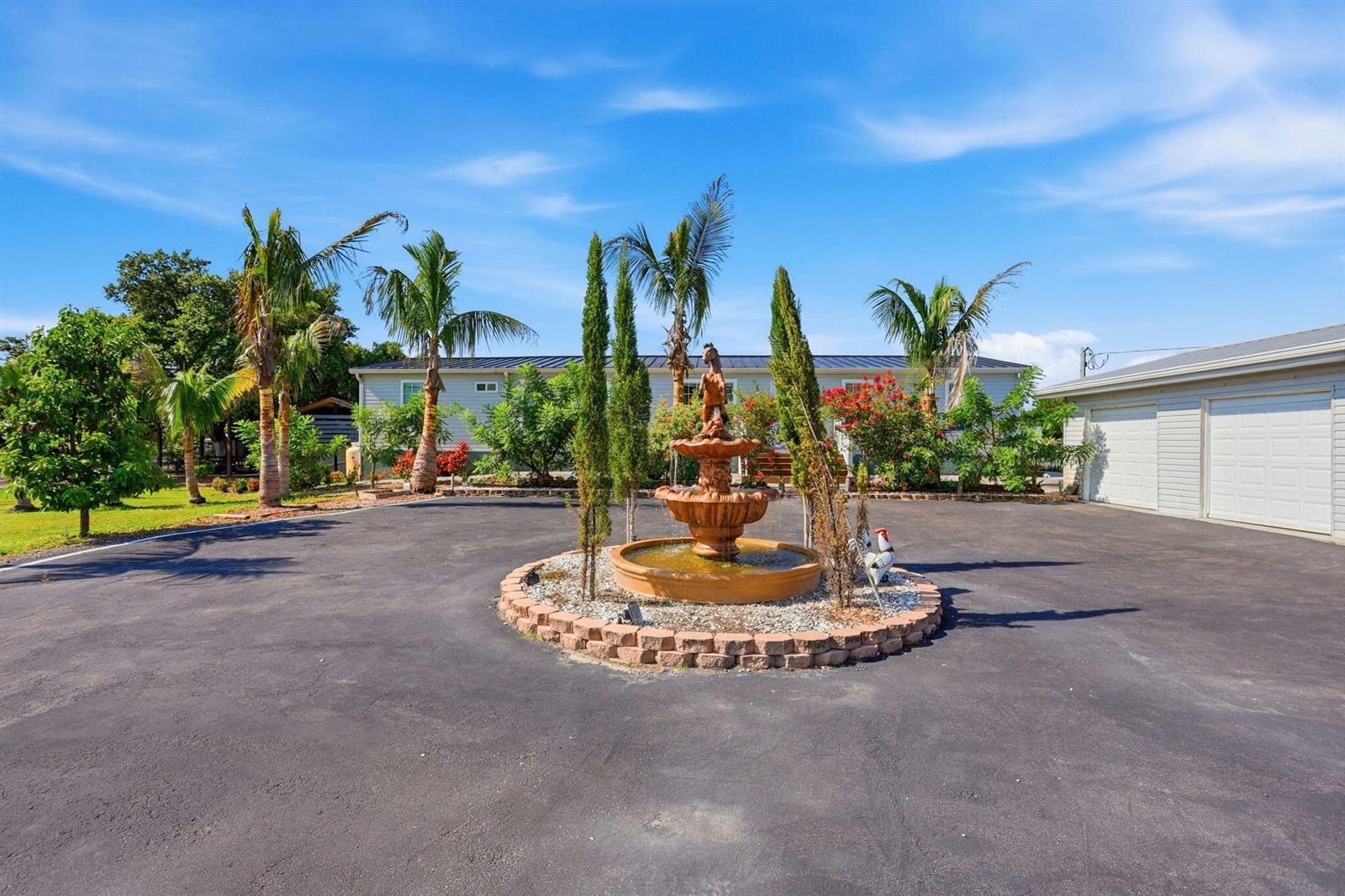 A tiered stone fountain sits in the center of a paved driveway before a house — 13311 Dancy Avenue, Clewiston FL 33440, CLEWISTON, FL