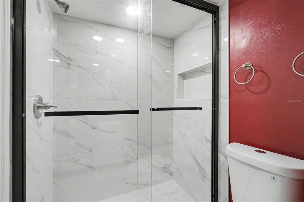 A walk-in shower with white marble-look tile and black hardware sits beside a red wall — 4505 LA CAPRI COURT, TAMPA, FL