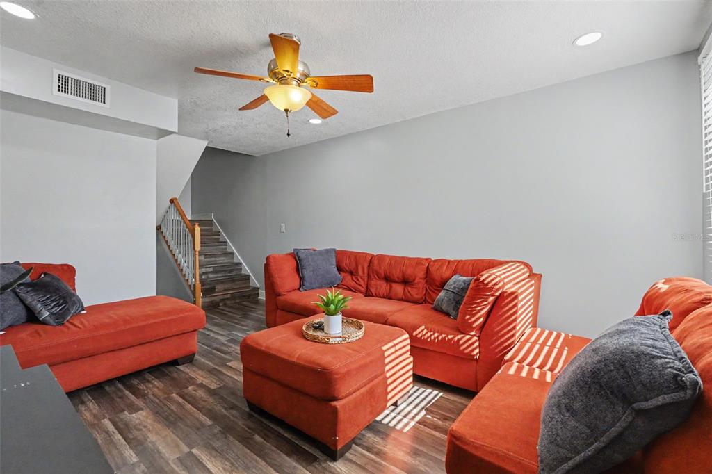 A living room features orange sectional seating, a matching ottoman, and wood-look flooring — 4505 LA CAPRI COURT, TAMPA, FL