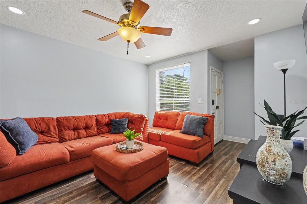 A living room features an orange sectional sofa, a matching ottoman, and wood-look flooring — 4505 LA CAPRI COURT, TAMPA, FL