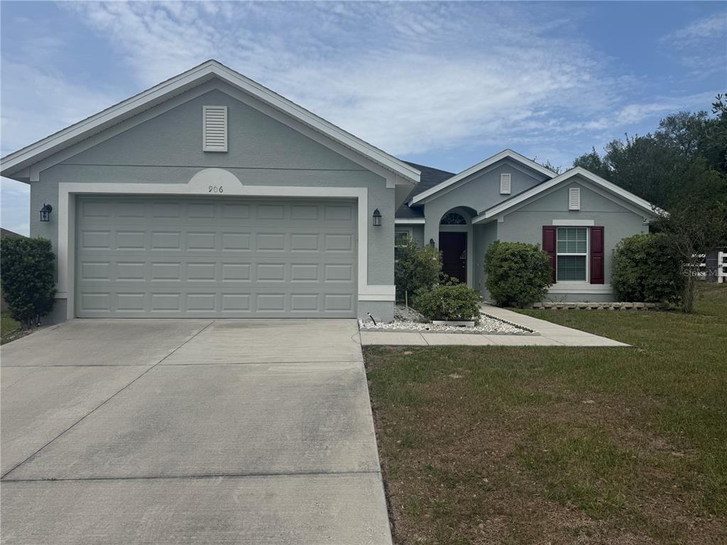 A single-story house with a gray exterior, a two-car garage, and red window shutters — 906 CHESTNUT DRIVE, FRUITLAND PARK, FL