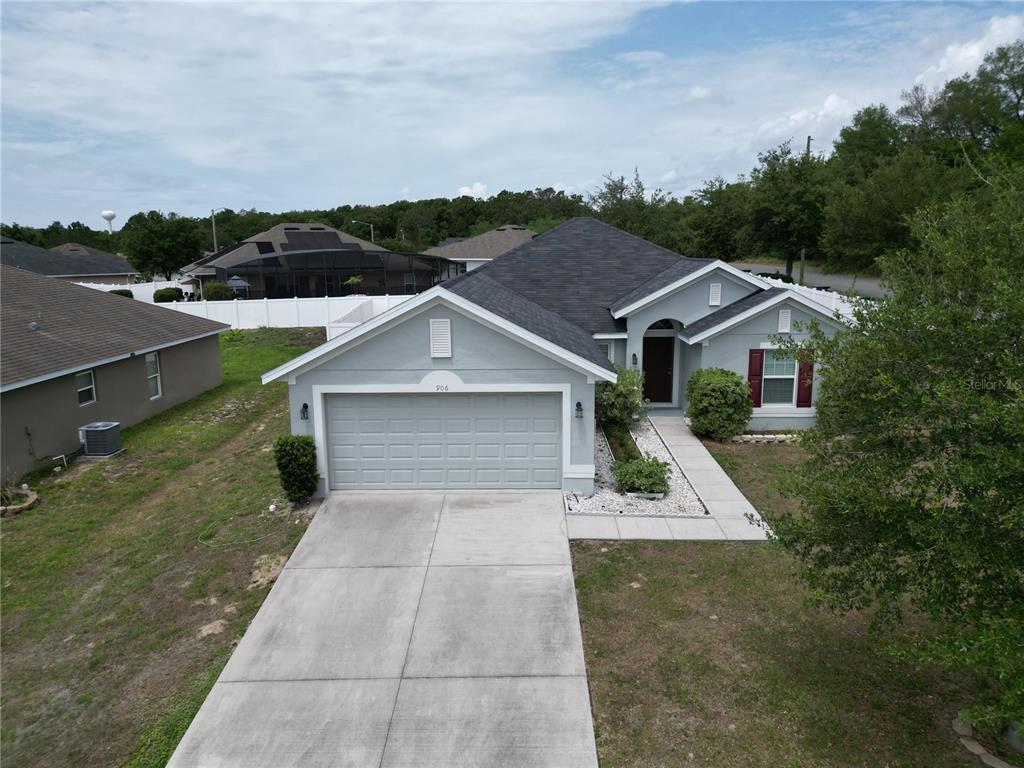 An aerial view of a single-story house with a gray exterior, garage, and concrete driveway — 906 CHESTNUT DRIVE, FRUITLAND PARK, FL