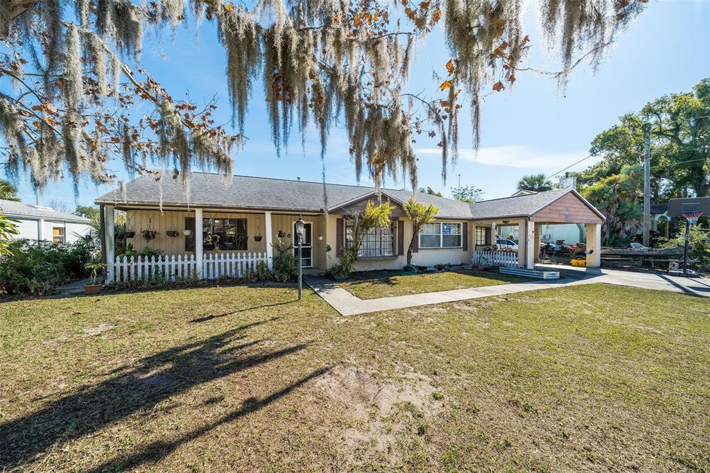 A single-story house with a white picket fence, a carport, and Spanish moss-covered trees — 708 N SAINT CLAIR ABRAMS AVENUE, TAVARES, FL