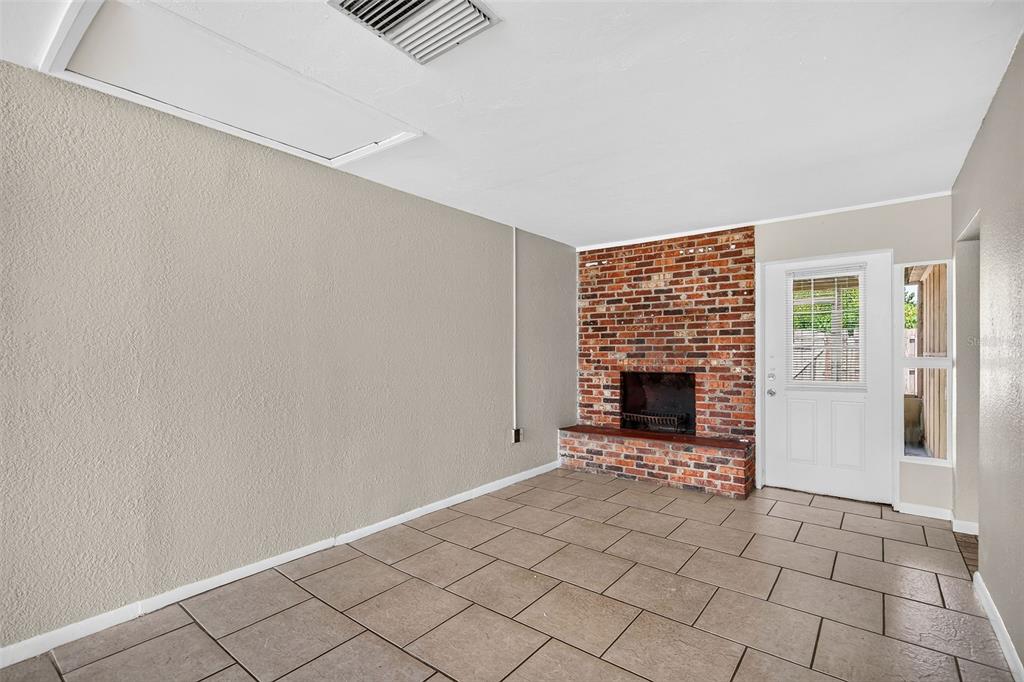 A room with tan walls, tiled floors, and a brick fireplace next to a white door — 708 N SAINT CLAIR ABRAMS AVENUE, TAVARES, FL