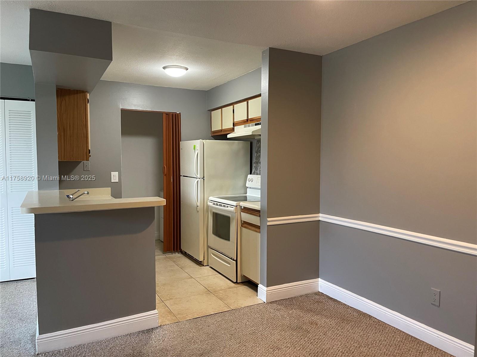 A kitchen with gray walls, a breakfast bar, and white appliances opens to a carpeted area — 1247 SW 46th Ave # 1312, Pompano Beach FL 33069, POMPANO BEACH, FL