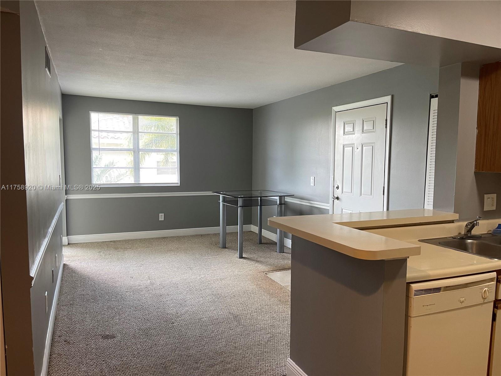 This room features gray walls, beige carpeting, a glass table, and a kitchen pass-through counter — 1247 SW 46th Ave # 1312, Pompano Beach FL 33069, POMPANO BEACH, FL