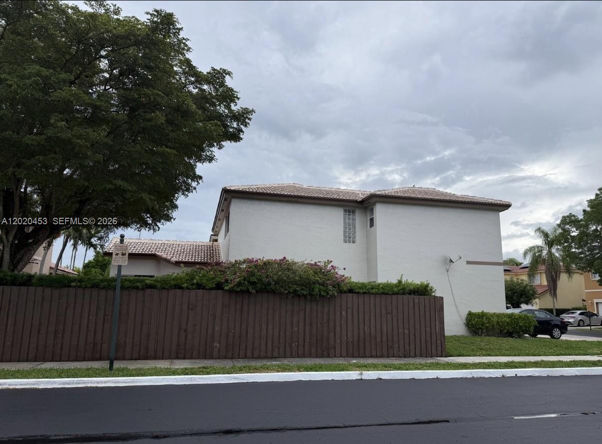 A two-story stucco building with a tile roof stands behind a wooden privacy fence — 15619 SW 112th Dr, Miami FL 33196, MIAMI, FL