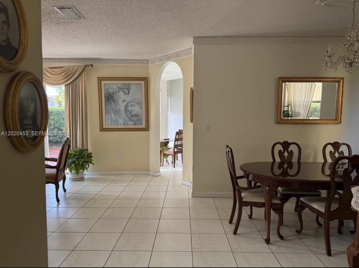 A dining room with tile floors, a round wooden table, and an arched doorway — 15619 SW 112th Dr, Miami FL 33196, MIAMI, FL
