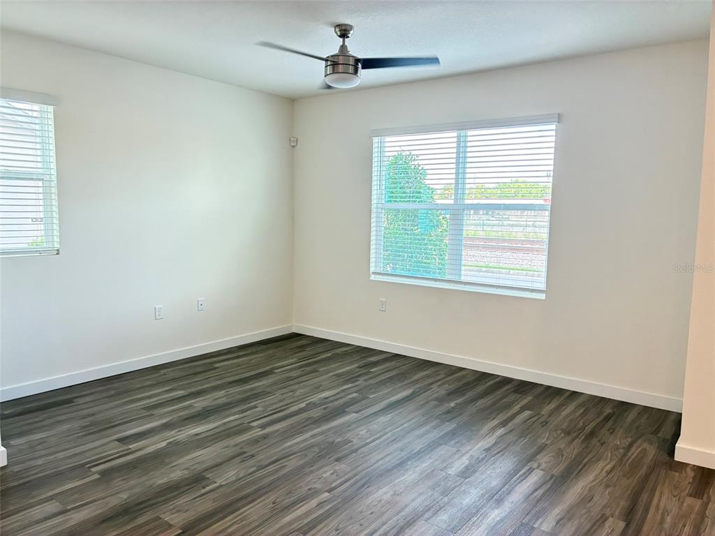 An empty bedroom features white walls, dark wood-look flooring, a ceiling fan, and two windows — 553 JOHN L MICA WAY, LONGWOOD, FL