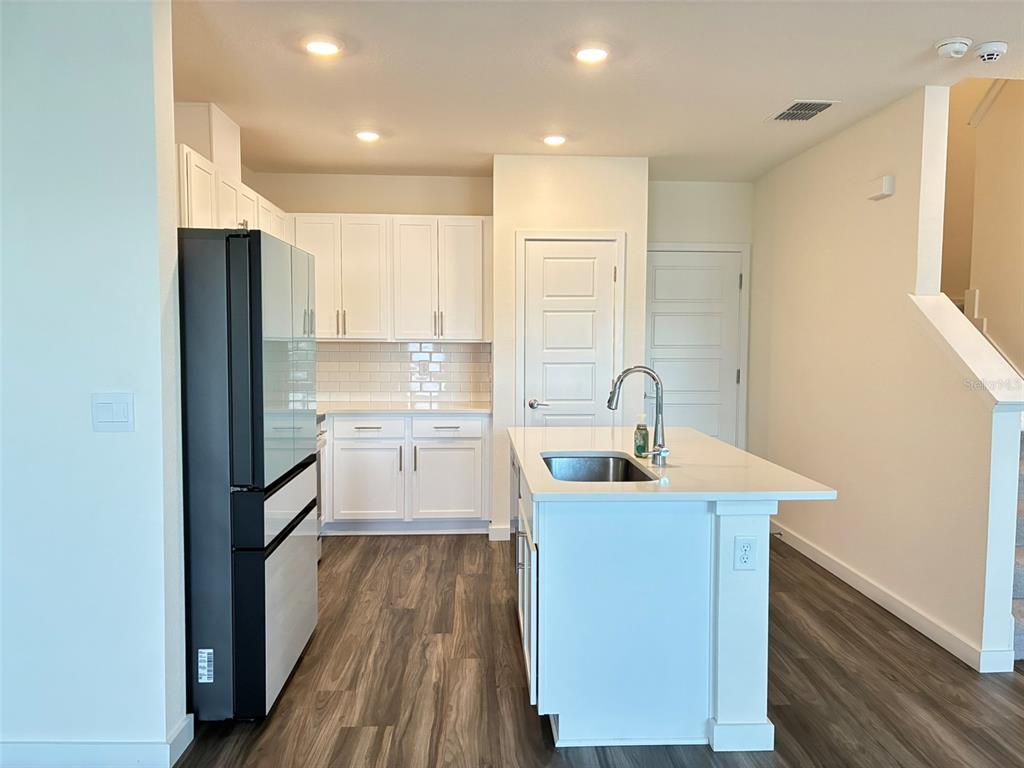 A modern kitchen features white cabinets, a central island with a sink, and wood-look flooring — 553 JOHN L MICA WAY, LONGWOOD, FL