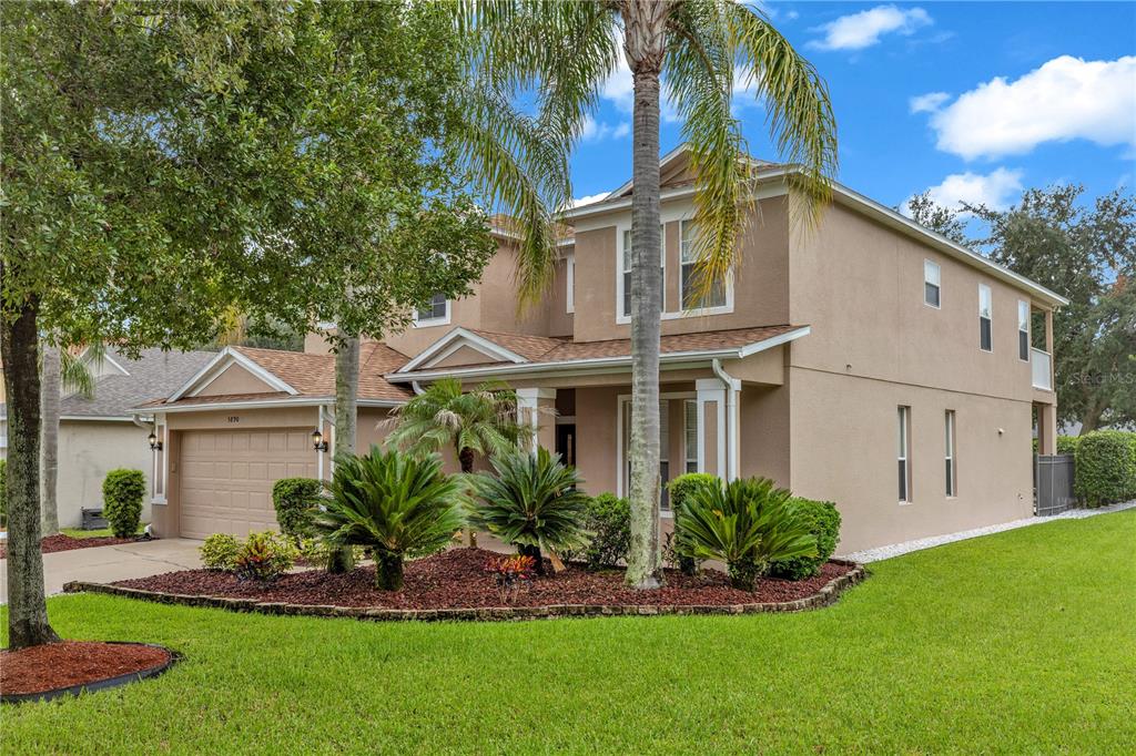 A two-story beige house with a two-car garage and manicured landscaping under a blue sky — 5890 ANSLEY WAY, MOUNT DORA, FL