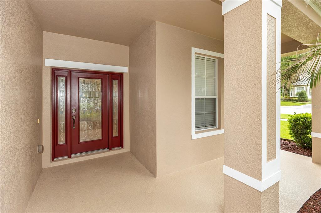 A covered front porch features a red door with glass inserts and a white column — 5890 ANSLEY WAY, MOUNT DORA, FL