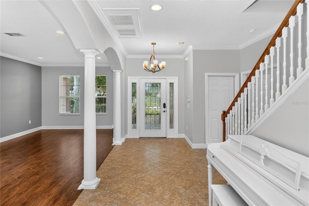 An entryway features tile flooring, a white staircase, a chandelier, and a view into a room — 5890 ANSLEY WAY, MOUNT DORA, FL