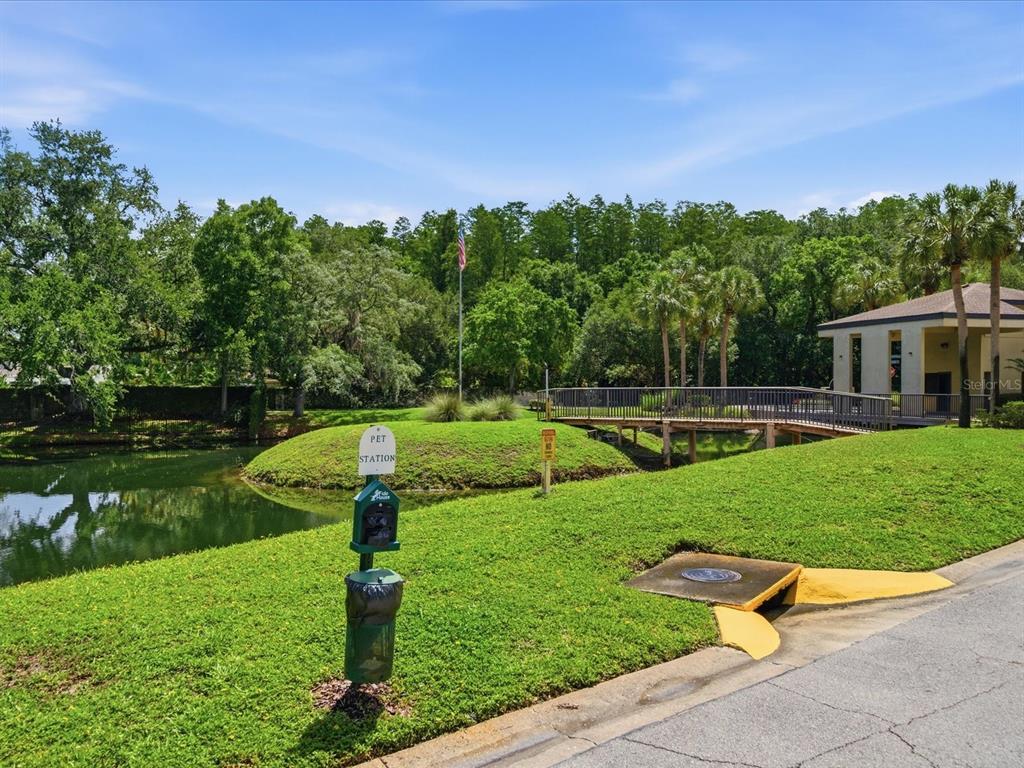 A pet waste station stands on a grassy lawn beside a pond and a footbridge — 13626 GREENFIELD DRIVE UNIT 401, TAMPA, FL