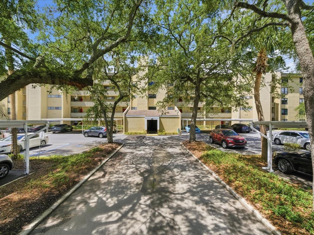 A multi-story apartment building with covered parking spaces and mature trees in the foreground — 13626 GREENFIELD DRIVE UNIT 401, TAMPA, FL