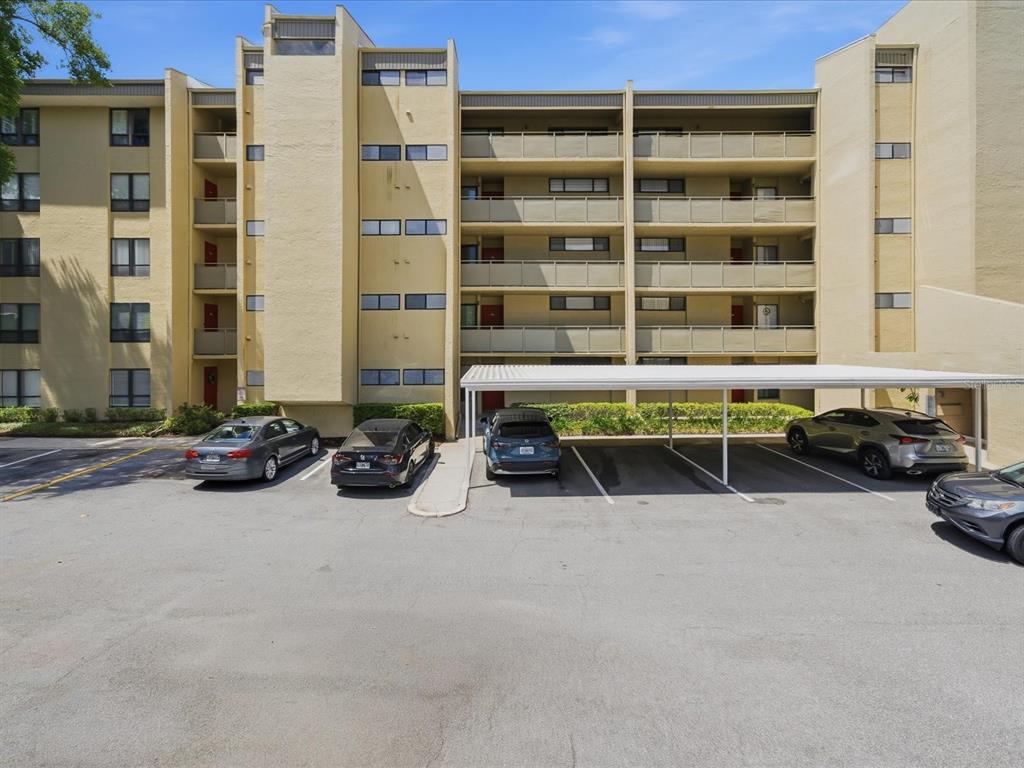 A multi-story apartment building with a parking lot and covered carports in front — 13626 GREENFIELD DRIVE UNIT 401, TAMPA, FL