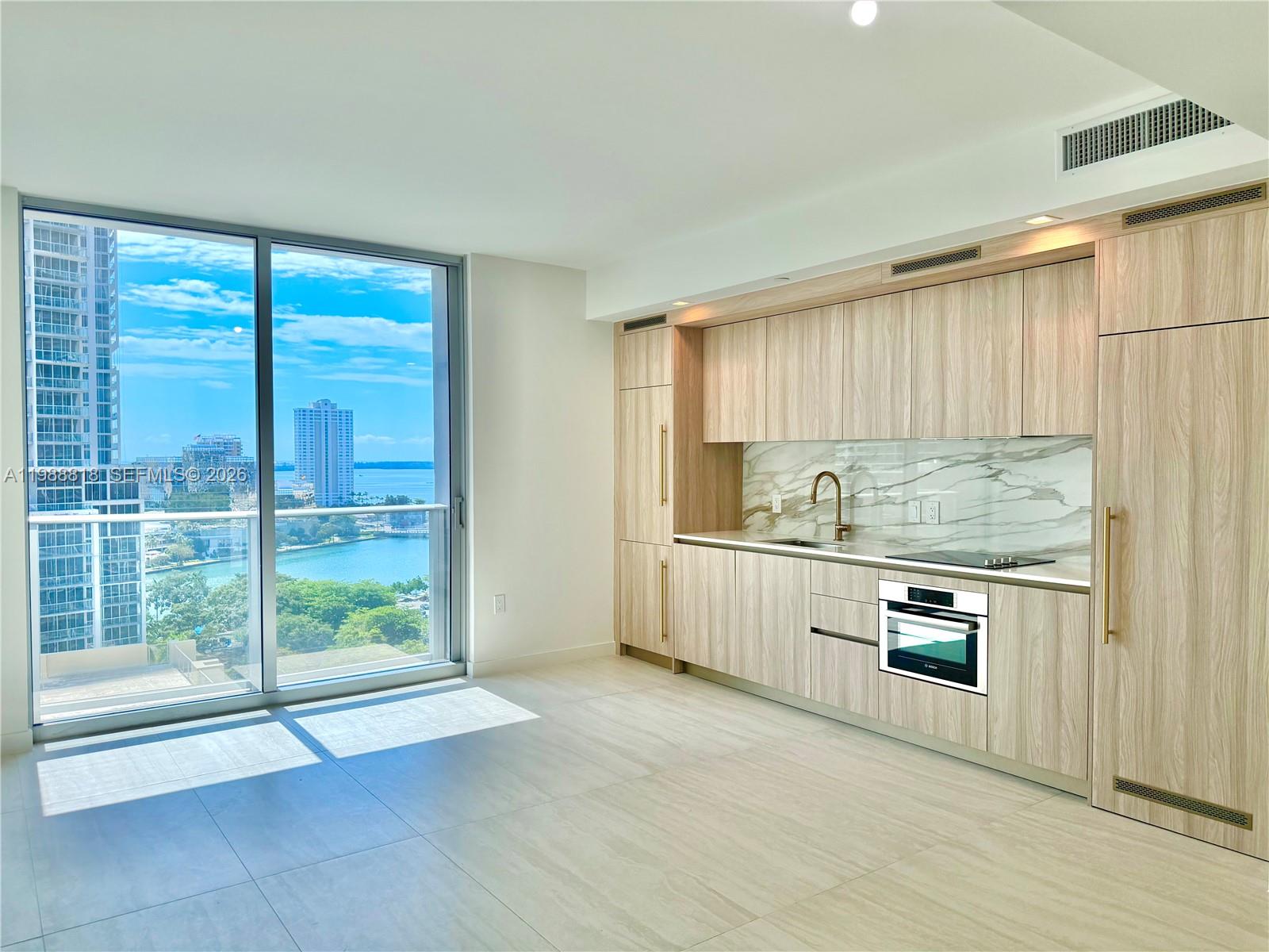 A modern kitchen with light wood cabinetry and marble backsplash overlooks a city waterfront view — 77 SE 5th St # 1615, Miami FL 33131, MIAMI, FL