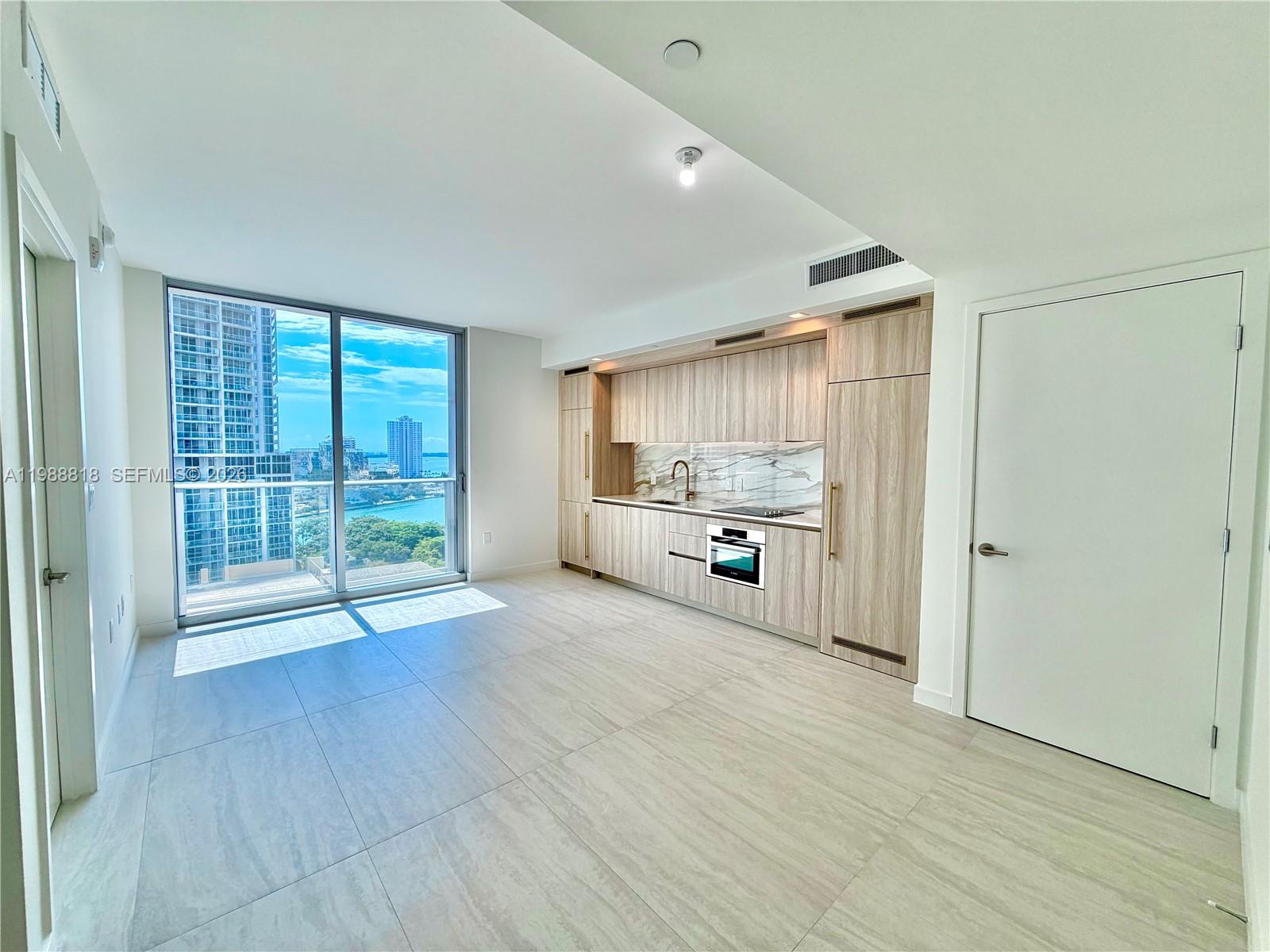 A modern kitchen with light wood cabinetry and marble backsplash overlooks a city waterfront view — 77 SE 5th St # 1615, Miami FL 33131, MIAMI, FL