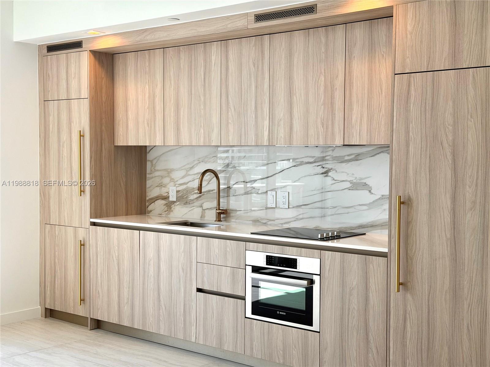 A modern kitchen features light wood cabinetry, a marble backsplash, and a built-in oven — 77 SE 5th St # 1615, Miami FL 33131, MIAMI, FL