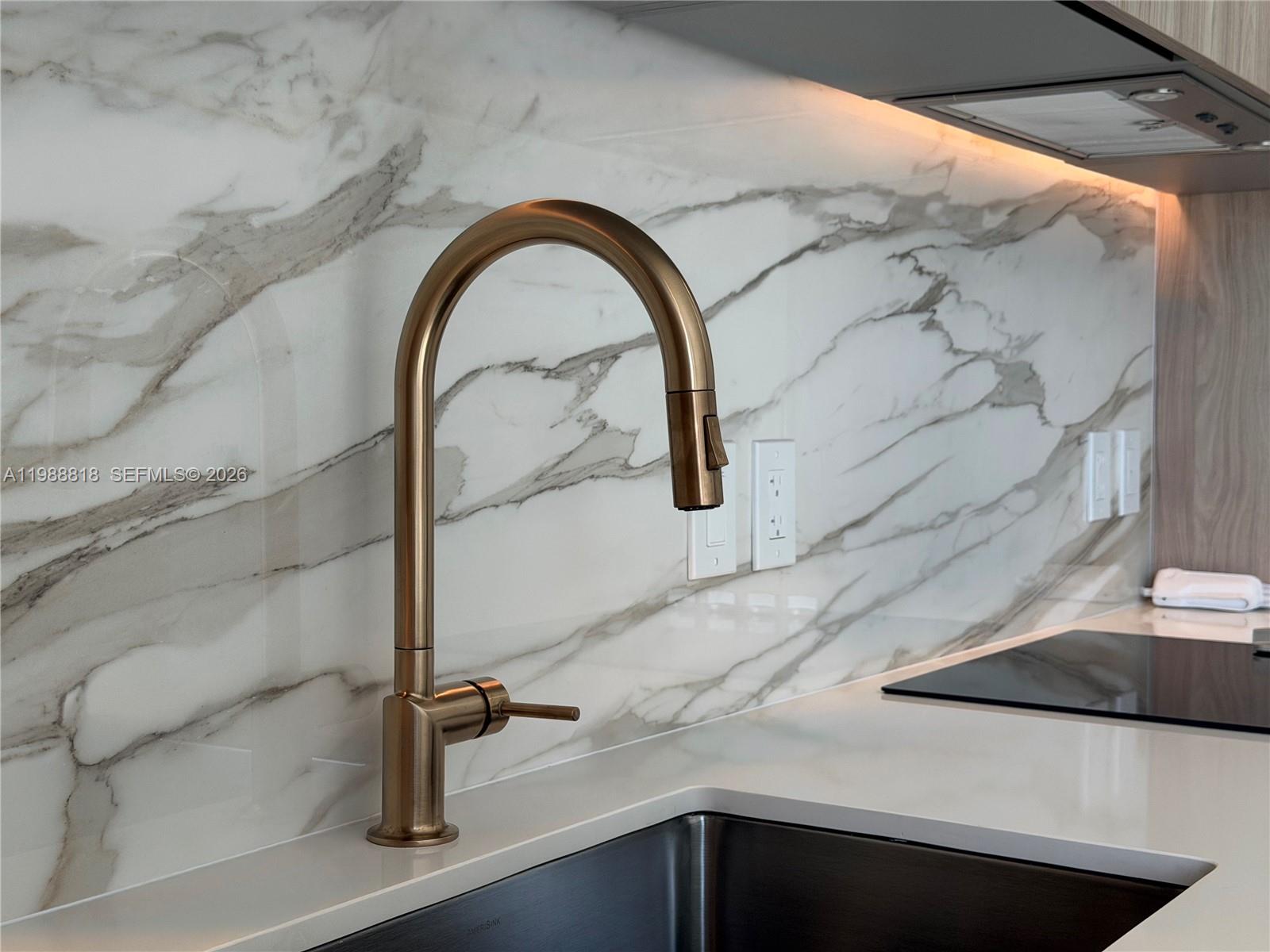 A modern kitchen features a bronze faucet, marble backsplash, and white countertop — 77 SE 5th St # 1615, Miami FL 33131, MIAMI, FL
