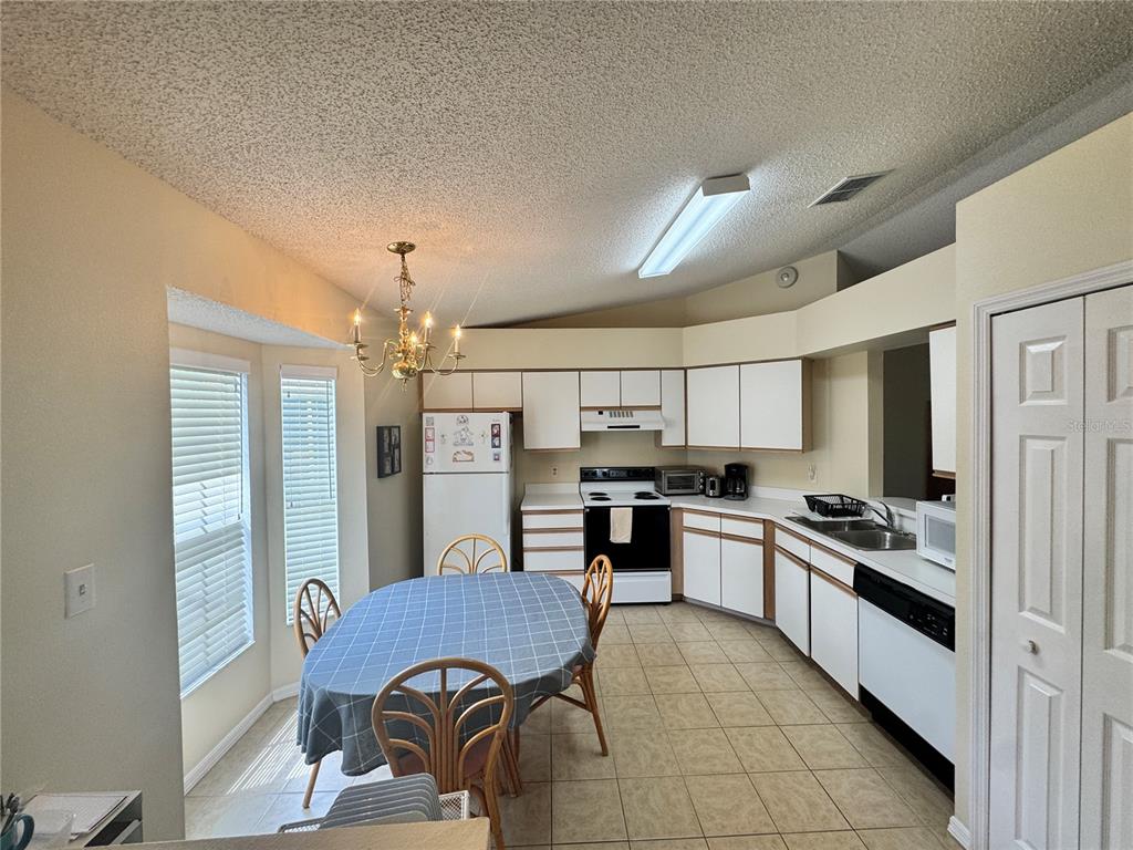 A kitchen with white cabinets, tile flooring, a dining table, and a vaulted ceiling — 25220 WILD HERON, LEESBURG, FL