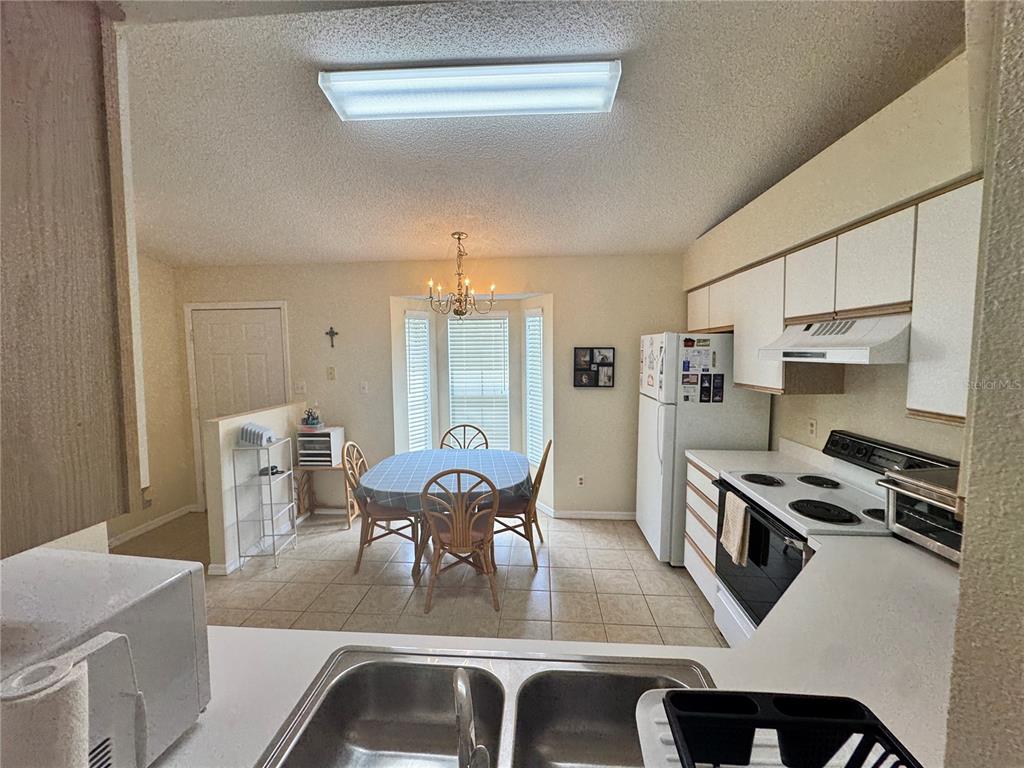 A kitchen with white cabinets and appliances overlooks a dining area with a bay window — 25220 WILD HERON, LEESBURG, FL