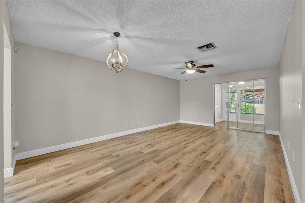 An empty room features light wood-look flooring, gray walls, a ceiling fan, and sliding glass doors — 2 VILLA VILLAR COURT UNIT 20, DELAND, FL