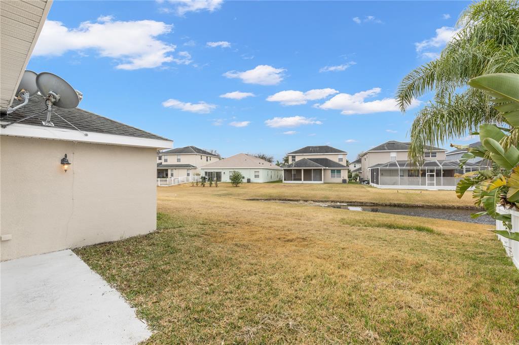 A view of a backyard with dry grass, a small pond, and neighboring suburban houses — 20011 NOB OAK AVENUE, TAMPA, FL