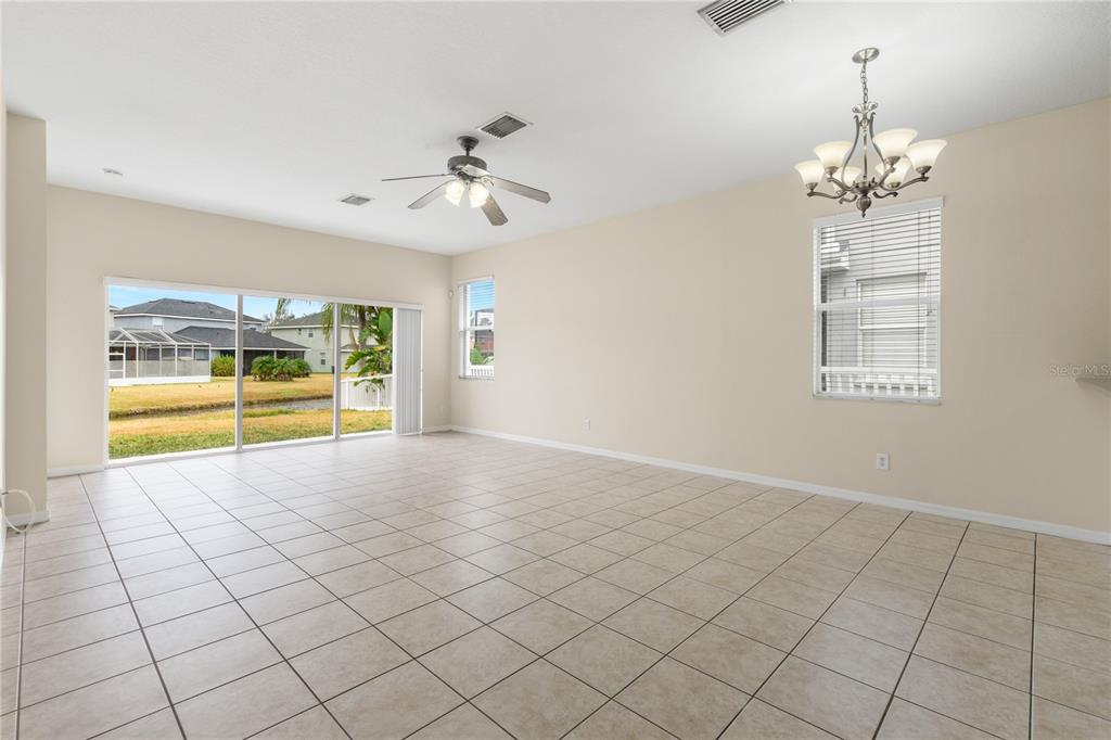 An empty living room features beige tile floors, a ceiling fan, and sliding glass doors — 20011 NOB OAK AVENUE, TAMPA, FL