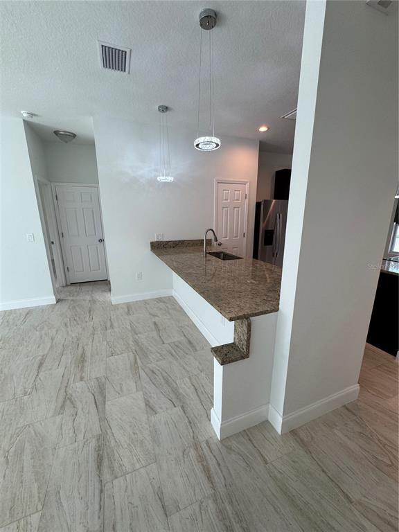 A kitchen features a granite breakfast bar, pendant lighting, and light-colored wood-look tile flooring — 2888 FOXDALE DRIVE, DELTONA, FL