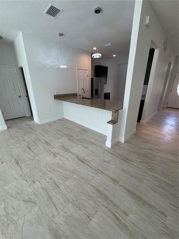 A kitchen features a granite breakfast bar, pendant lighting, and light-colored tile flooring — 2888 FOXDALE DRIVE, DELTONA, FL