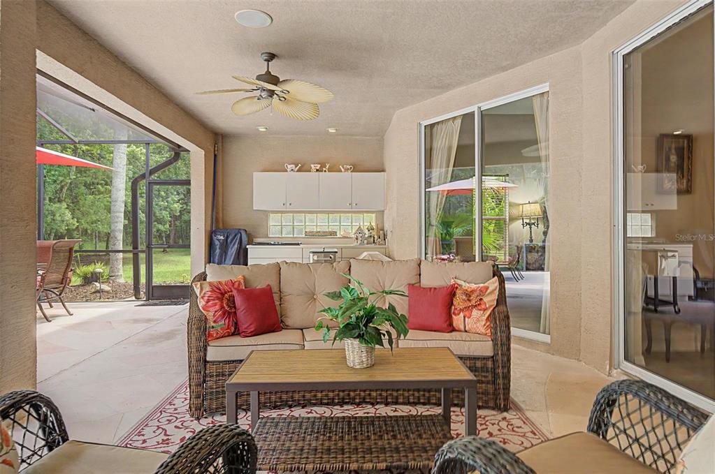 A covered patio features a wicker sofa, coffee table, outdoor kitchen, and a screened enclosure — 12146 WALSTONE COURT, TRINITY, FL