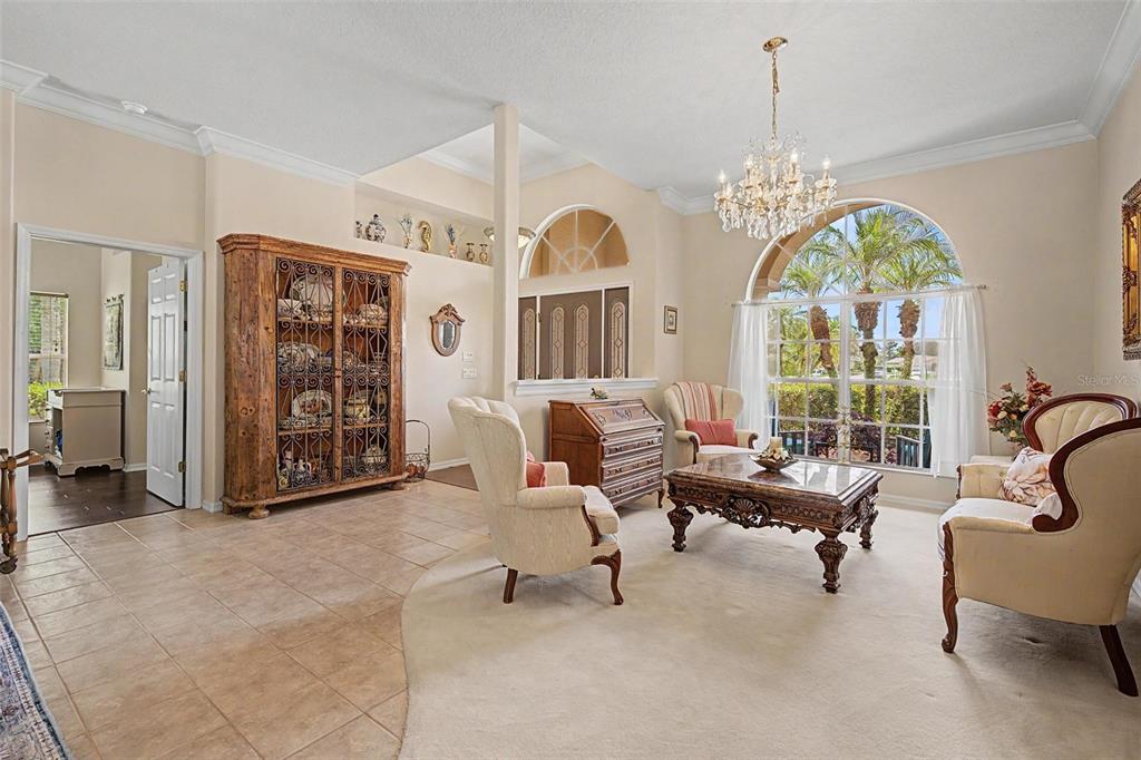 A living room features a crystal chandelier, arched window, tile and carpet flooring, and furniture — 12146 WALSTONE COURT, TRINITY, FL