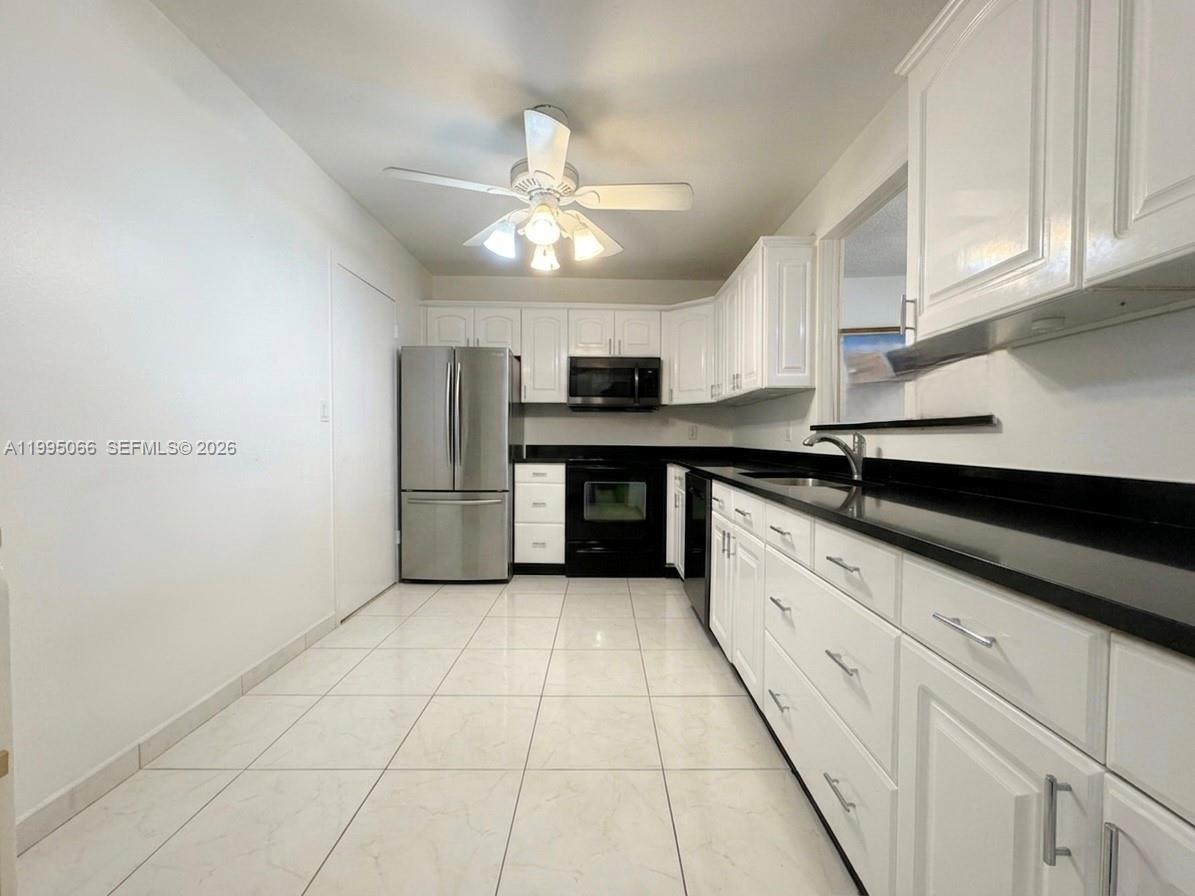 A kitchen features white cabinets, black countertops, stainless steel appliances, and light-colored tile flooring — 3800 S Ocean Dr # 816, Hollywood FL 33019, HOLLYWOOD, FL