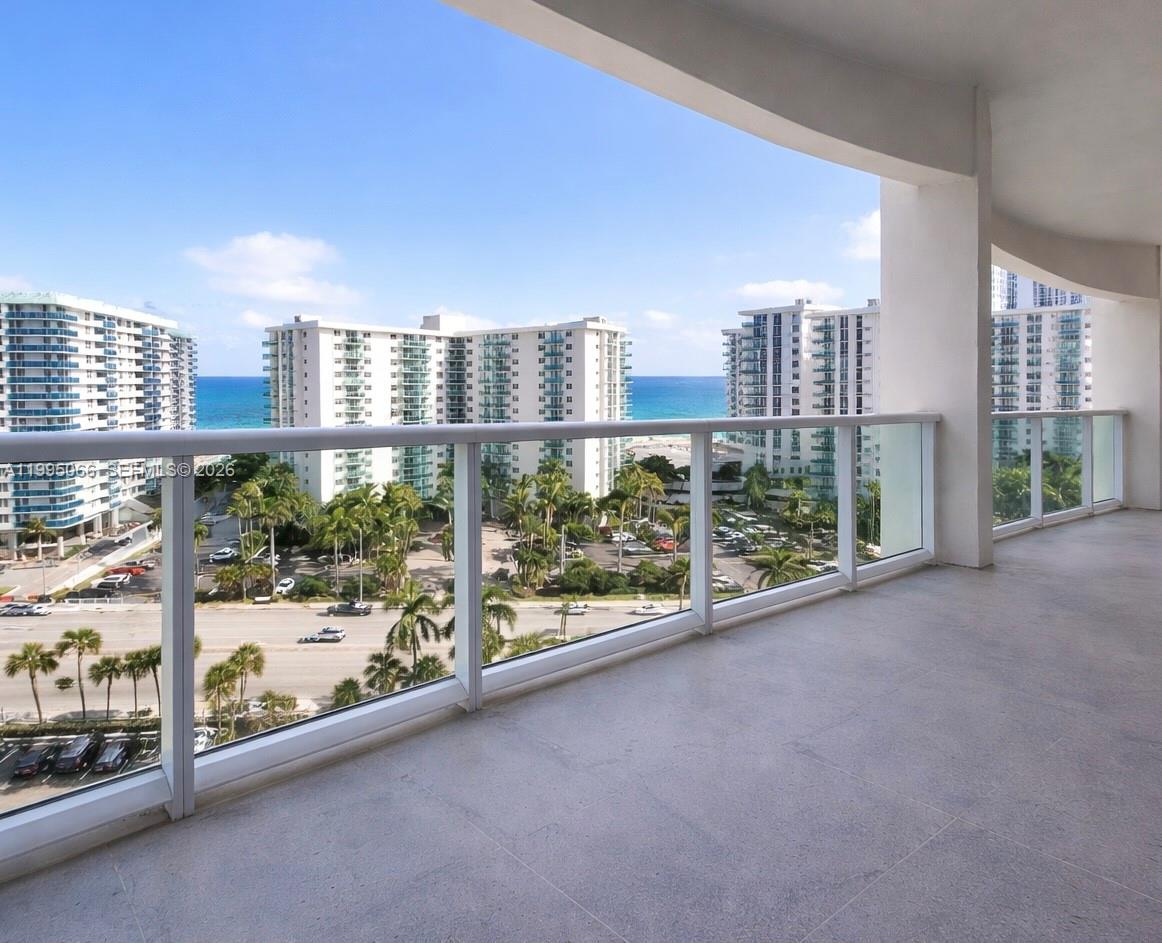 A spacious balcony with glass railings overlooks a coastal street, palm trees, and ocean views — 3800 S Ocean Dr # 816, Hollywood FL 33019, HOLLYWOOD, FL