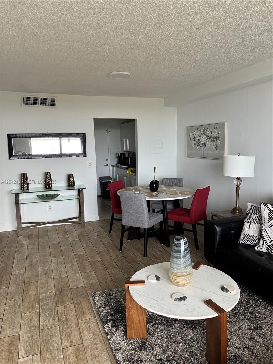 A living and dining area features wood-look tile flooring, a round table, and modern furniture — 2000 NE 135th St # 710, North Miami FL 33181, NORTH MIAMI, FL
