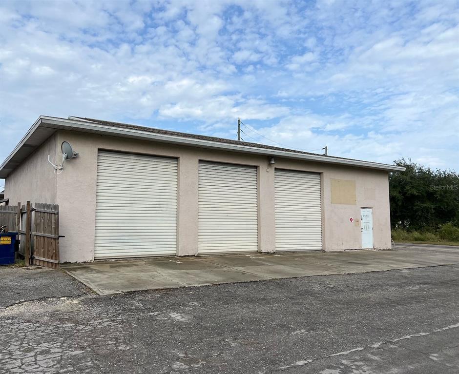 A single-story commercial building with three roll-up garage doors and a side entrance door — 7809 CLARK MOODY BOULEVARD, PORT RICHEY, FL