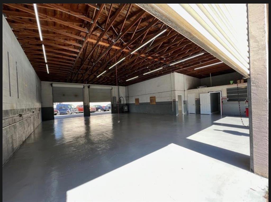 An empty warehouse space with a concrete floor, exposed wood ceiling, and two roll-up doors — 7809 CLARK MOODY BOULEVARD, PORT RICHEY, FL