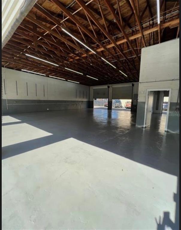 An empty industrial warehouse space with a concrete floor, exposed wood ceiling, and roll-up doors — 7809 CLARK MOODY BOULEVARD, PORT RICHEY, FL