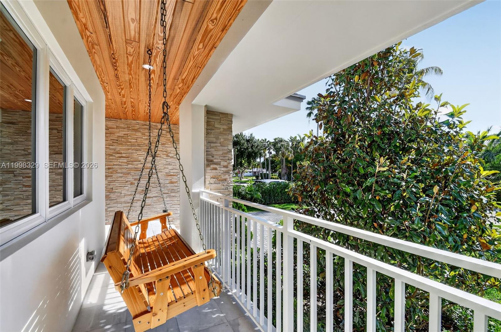A wooden porch swing hangs on a balcony with a wood-paneled ceiling and stone wall — 1017 S Palmway, Lake Worth FL 33460, LAKE WORTH, FL