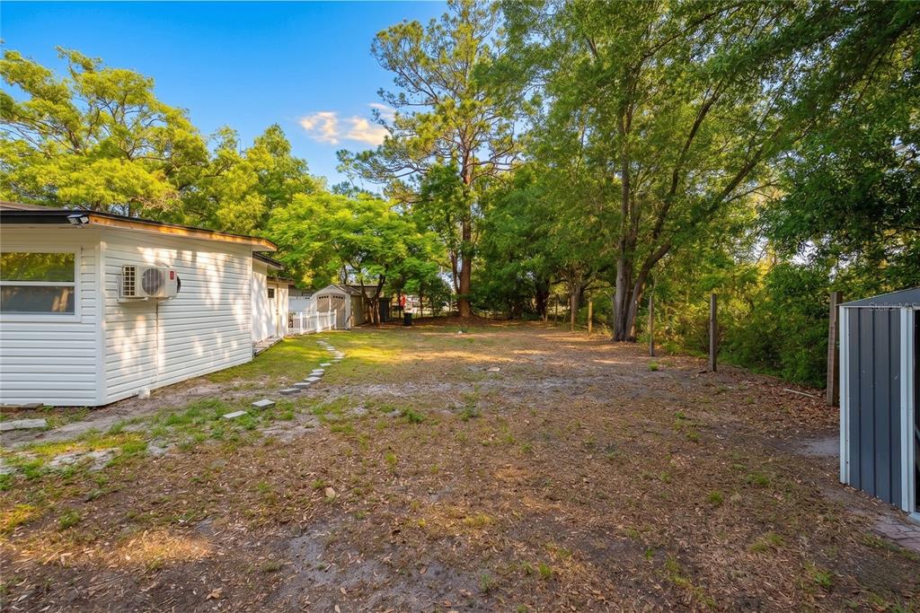 A grassy backyard features a white house, a small storage shed, and mature trees — 291 IVEY ROAD, CASSELBERRY, FL