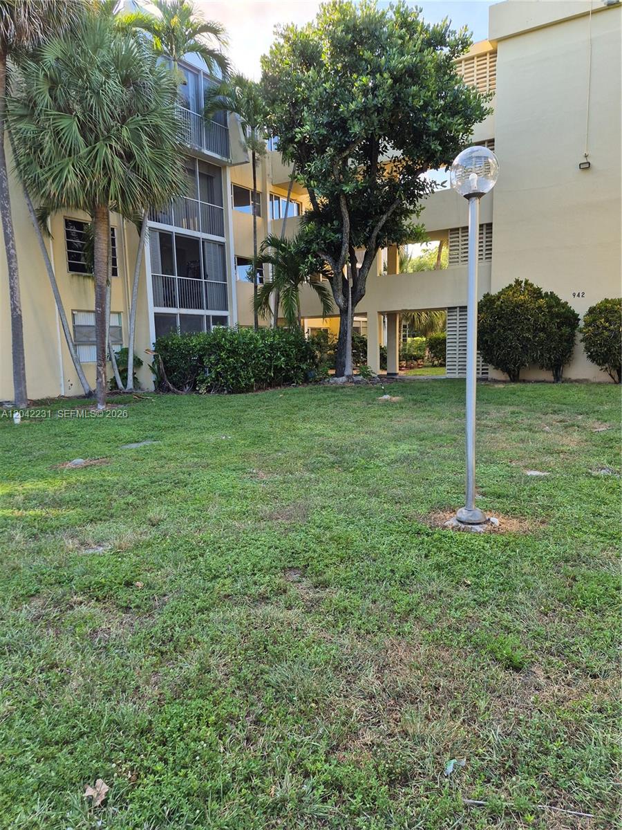 A multi-story apartment building exterior features a grassy lawn, palm trees, and a street lamp — 942 NE 199th St # 4G, Miami FL 33179, MIAMI, FL
