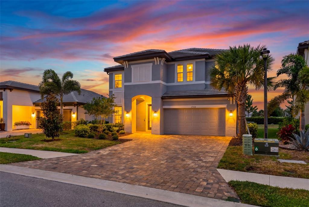 A two-story gray house with a paved driveway and palm trees at sunset — 17510 SAVORY MIST CIRCLE, BRADENTON, FL